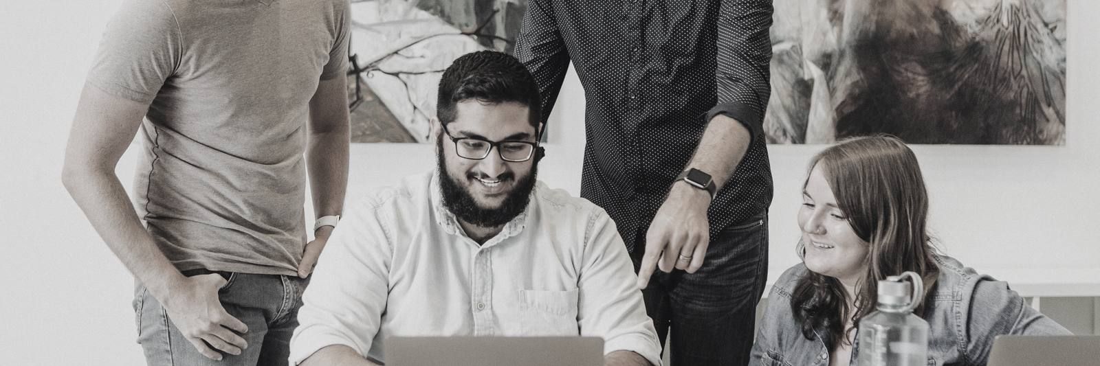 Four smiling colleagues around a laptop